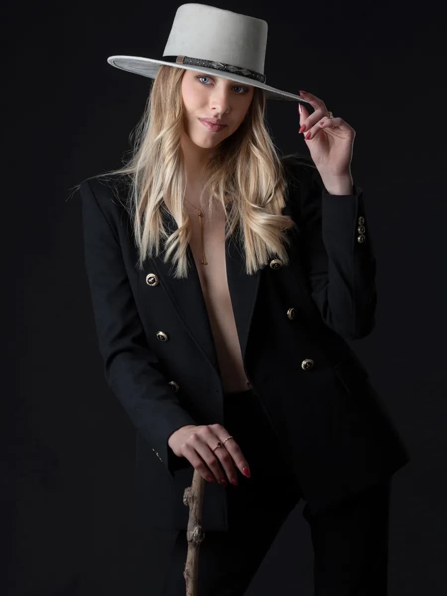 Femme blonde en costume noir et chapeau clair, en studio