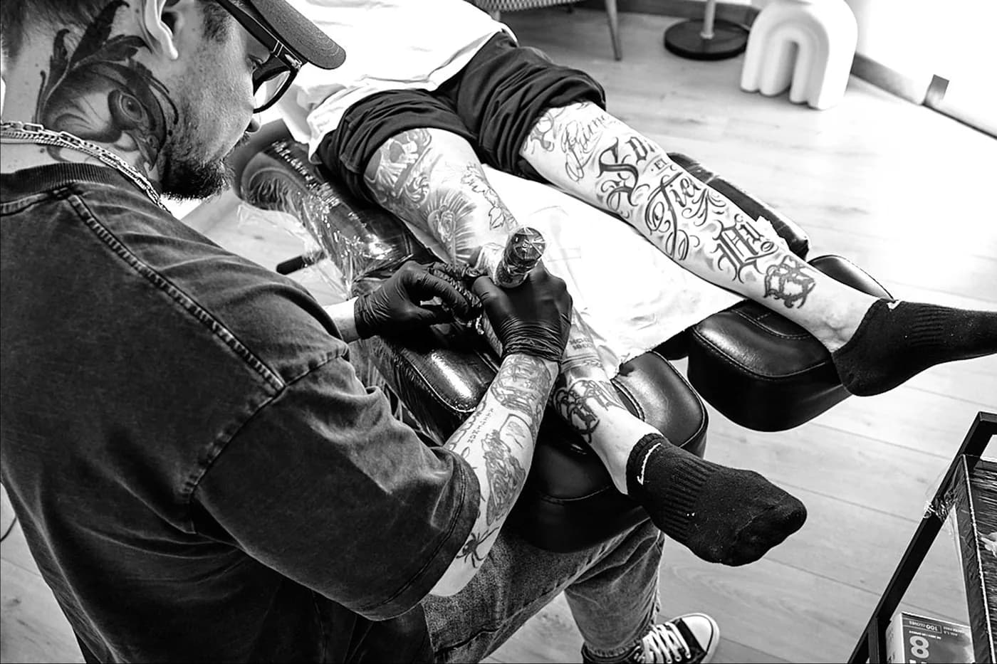 Tatoueur au travail sur la jambe d’un client, en noir et blanc