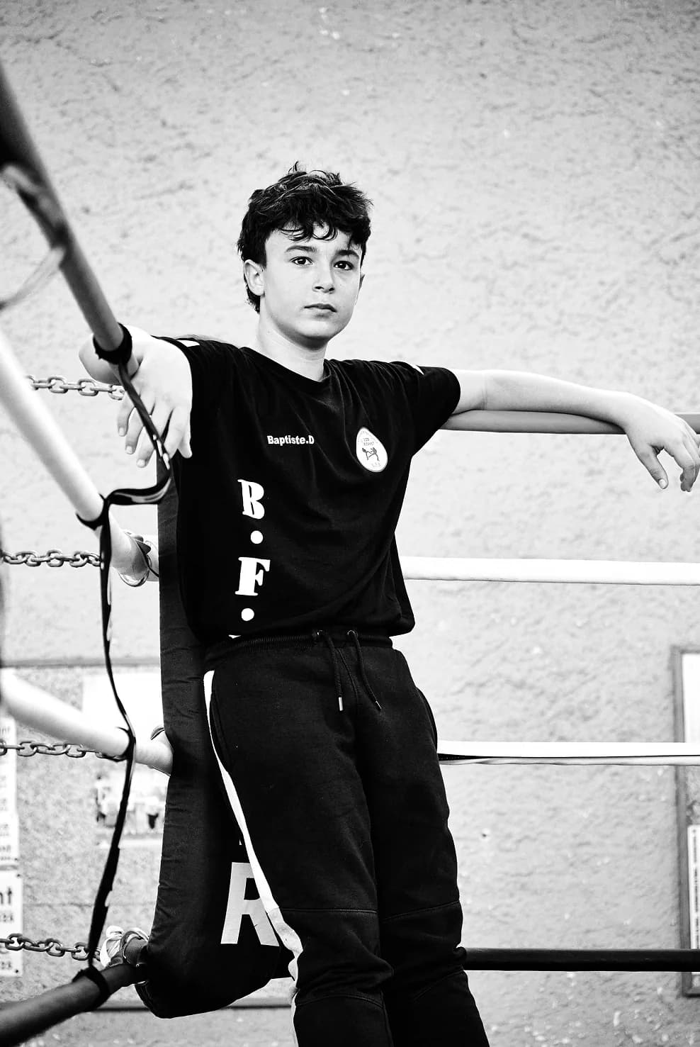 Jeune boxeur en tenue de club, accoudé aux cordes du ring, en noir et blanc