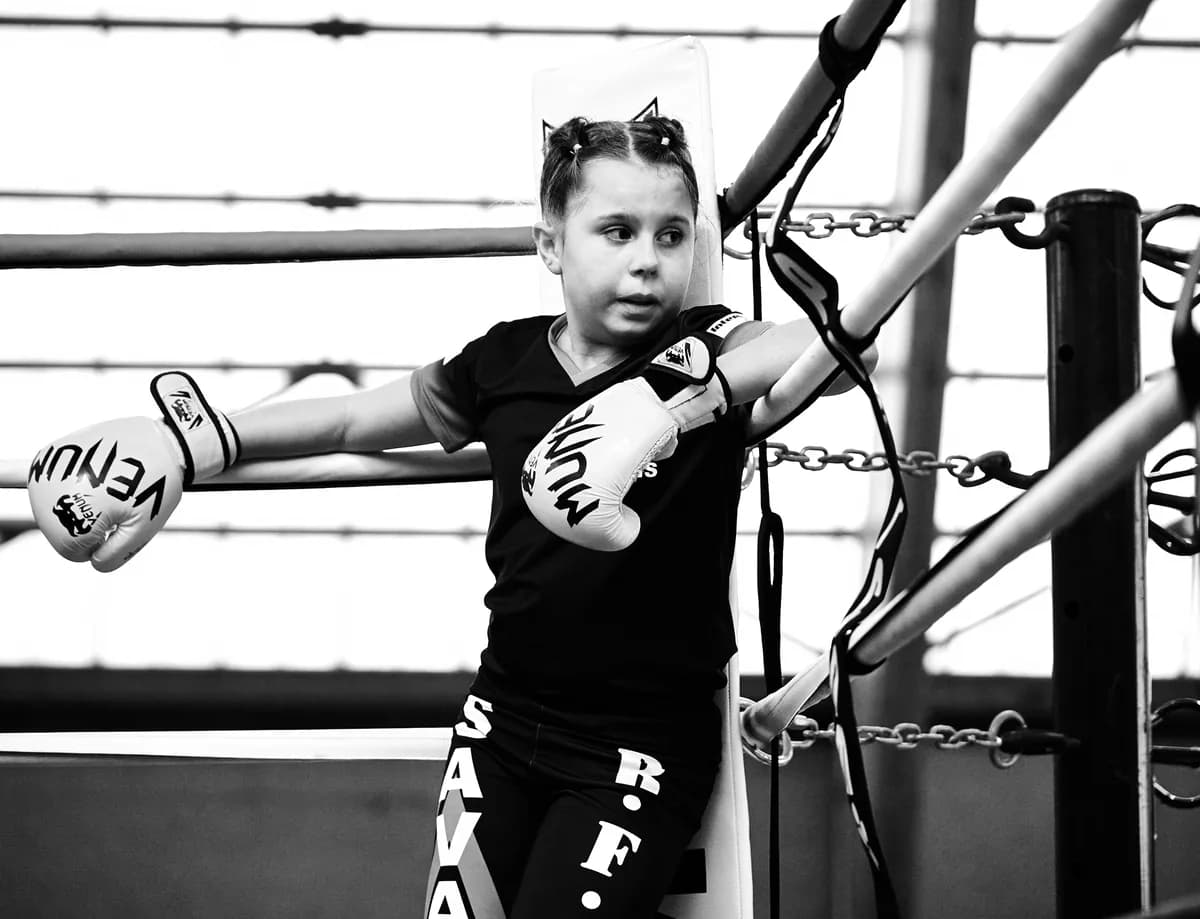 Jeune boxeuse gantée appuyée dans le coin du ring, en noir et blanc